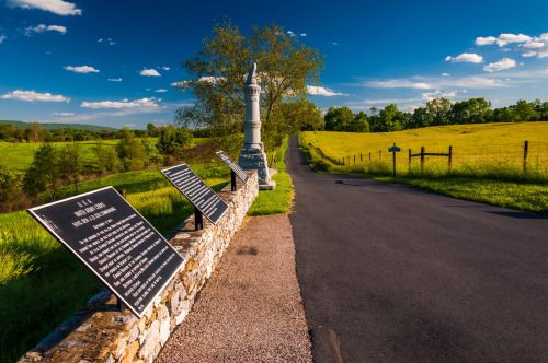 A scenic view of a road lined with historical markers, surrounded by green fields and blue skies.