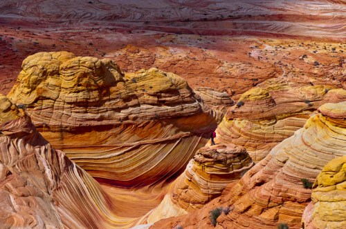 A person stands on a rock formation in a colorful, layered desert landscape with swirls of red, orange, and yellow.