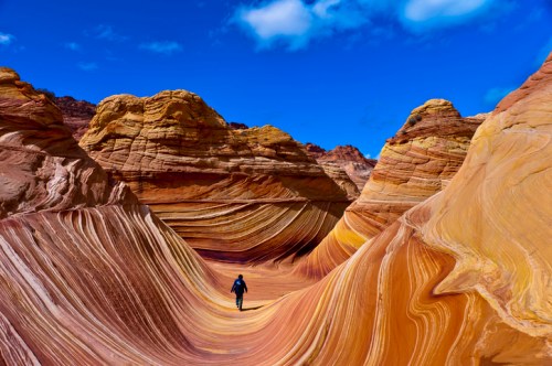 A person walks through colorful, swirling rock formations under a bright blue sky.