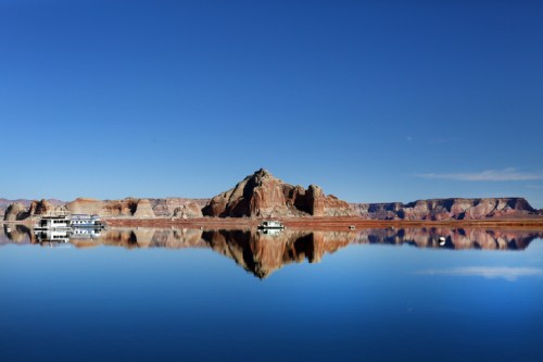 A serene lake reflects a rocky mountain under a clear blue sky, with boats anchored nearby.