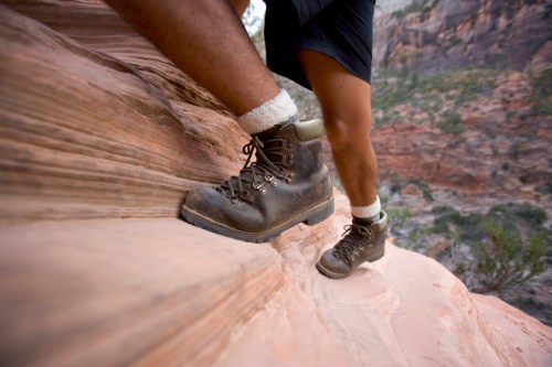A close-up of a hiker's boot on a rocky surface, with a leg visible and a scenic canyon backdrop.
