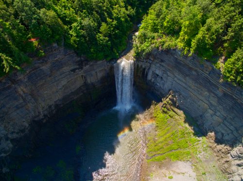 Aerial view of a waterfall cascading into a rocky pool, surrounded by lush green trees and cliffs.