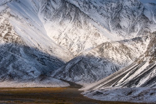 Snow-covered mountains with dramatic peaks and valleys, illuminated by soft sunlight, creating a serene landscape.