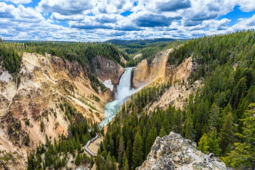 A stunning view of a waterfall cascading into a canyon, surrounded by lush green forests and dramatic clouds above.