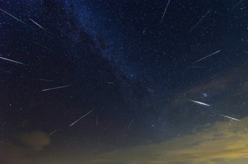 A starry night sky filled with numerous shooting stars and the Milky Way galaxy in the background.