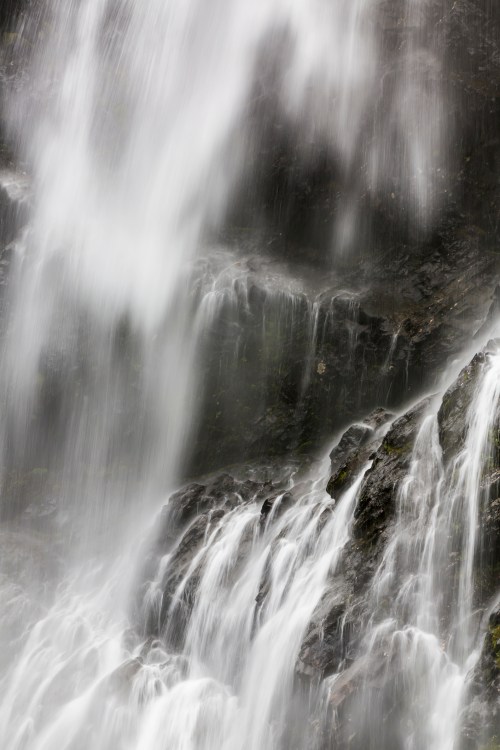 A close-up of cascading water flowing over dark rocks, creating a misty, ethereal effect.