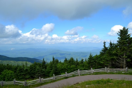 A scenic mountain view with rolling hills, a wooden fence, and a partly cloudy sky.