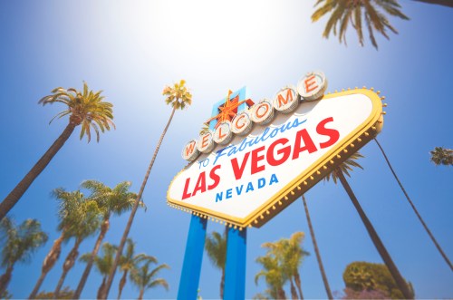 A colorful "Welcome to Fabulous Las Vegas" sign surrounded by palm trees against a bright blue sky.