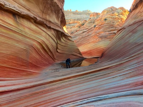 A photographer captures the colorful, wavy rock formations of The Wave in Arizona, surrounded by stunning natural beauty.