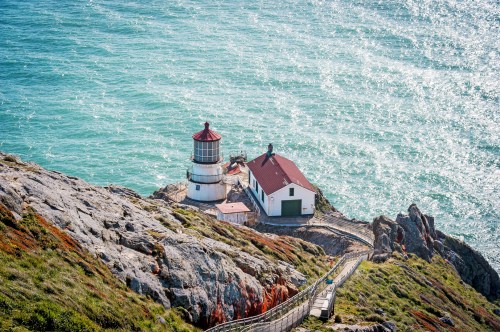 A scenic lighthouse on a rocky coastline, surrounded by vibrant greenery and sparkling blue ocean waves.