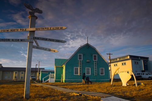 A turquoise building with directional signs, set against a cloudy sky, in a remote location with a person and child.