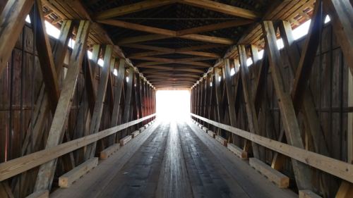 A wooden covered bridge with a bright light at the end, showcasing intricate wooden beams and a long pathway.