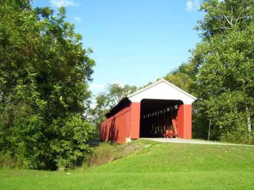 A red covered bridge surrounded by green trees under a clear blue sky.