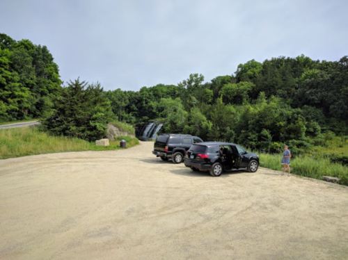 Two SUVs parked on a dirt road near a lush green area with a waterfall in the background and a person standing nearby.