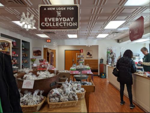 A cozy shop interior featuring holiday decorations, displays of baked goods, and customers browsing the collection.
