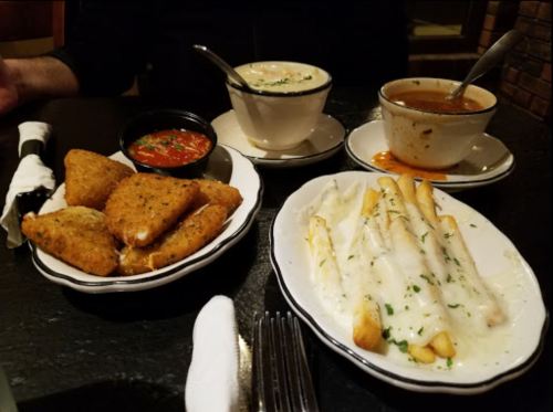 A table setting with fried appetizers, creamy soup, and cheesy pasta, garnished with herbs and served in bowls.