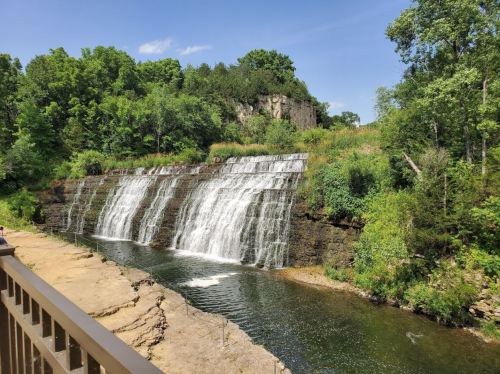 A scenic view of a waterfall cascading over rocky cliffs, surrounded by lush greenery and a clear blue sky.