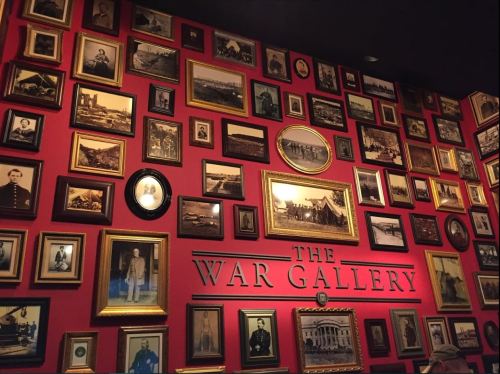 A wall covered with framed historical photographs and portraits, labeled "The War Gallery."