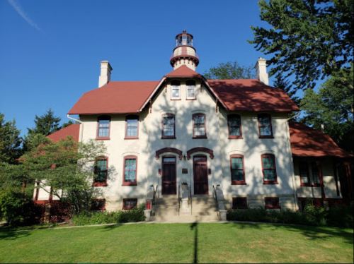 Historic building with a red roof and lighthouse-style tower, surrounded by trees and a grassy area.