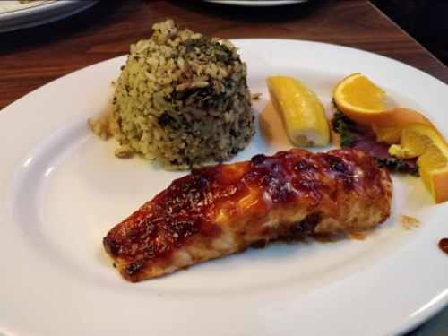 A plate featuring glazed salmon, herbed rice, lemon, and orange slices, garnished with greens.
