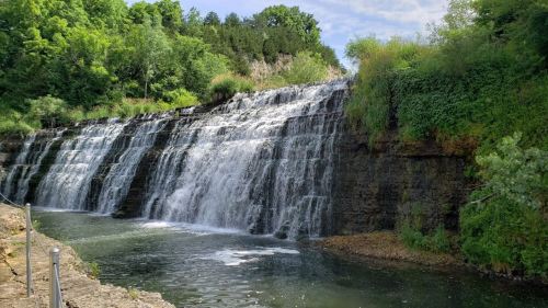 A serene waterfall cascading over rocky cliffs into a calm pool, surrounded by lush greenery and trees.