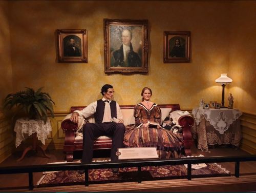 A historical diorama featuring a man and woman seated on a couch, surrounded by vintage decor and portraits.