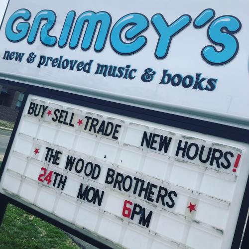 Sign for Grimey's, advertising new hours and an event featuring The Wood Brothers on Monday at 6 PM.
