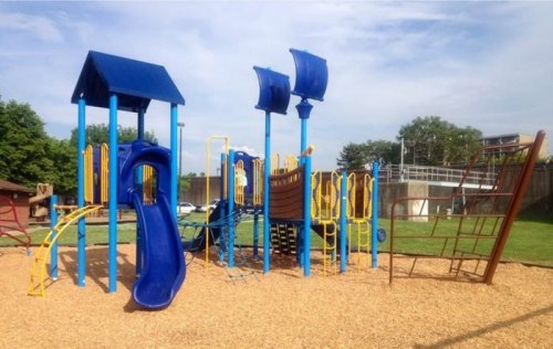 Colorful playground equipment with slides, climbing structures, and a ship-like design, set on a grassy area.