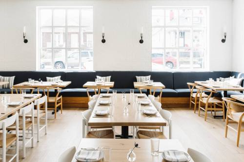 Bright, modern restaurant interior with wooden tables, white chairs, and a cozy seating area by the windows.
