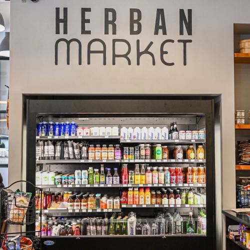 A display shelf in a store labeled "Herban Market," filled with various beverages and products.
