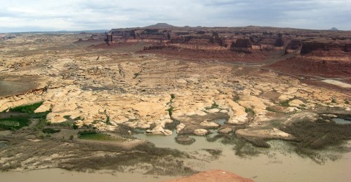 A vast desert landscape with rocky formations and a winding river, under a cloudy sky.