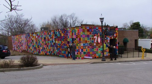 Colorful mural covering a building exterior, with people walking nearby and a cloudy sky above.