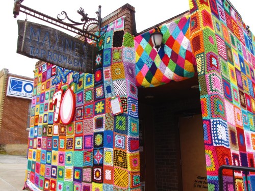 Colorful yarn art covers the exterior of Maxine's Tap Room & Bar, creating a vibrant, inviting atmosphere.