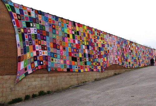 A colorful patchwork quilt drapes over a wall, featuring various patterns and designs in vibrant hues.