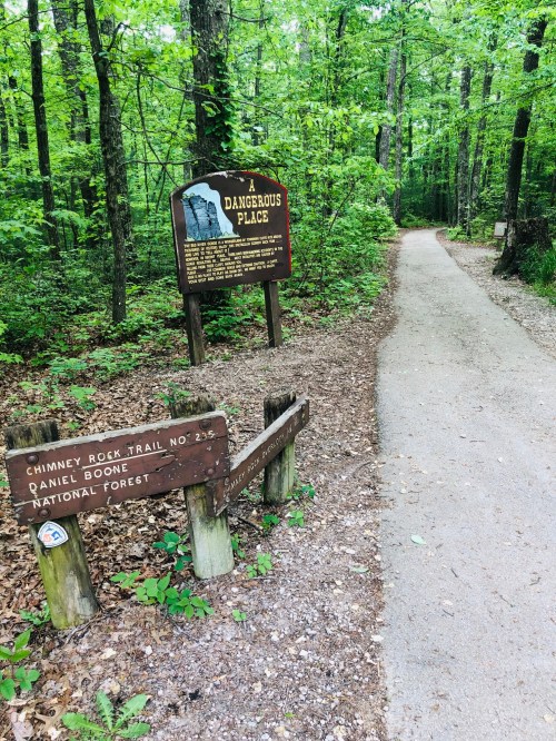 A wooded trail in a national forest with signs for Chimney Rock Trail and a warning about a dangerous area.