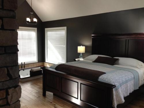 Cozy bedroom with a dark accent wall, large bed, bedside lamp, and windows letting in natural light.