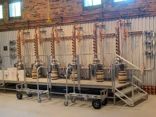 A distillation setup featuring multiple copper stills and barrels in a brick-walled industrial space.