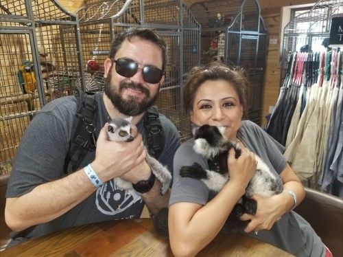 A man and woman smile while holding small animals in a cozy indoor setting with animal cages in the background.