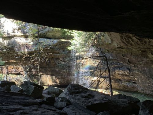 A view from a cave entrance, showcasing a waterfall and lush greenery in a rocky landscape.