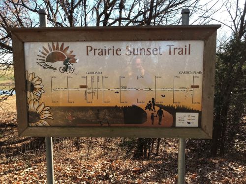 Sign for Prairie Sunset Trail featuring a map, sun graphic, and illustrations of flowers and cyclists.