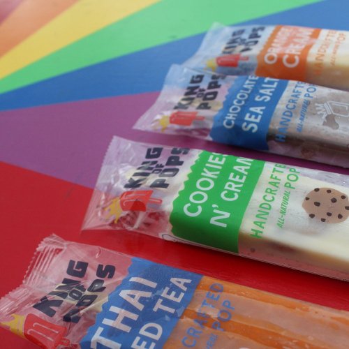 Colorful rainbow background featuring various handcrafted popsicles in clear packaging. Flavors include Thai Iced Tea and Cookie N' Cream.