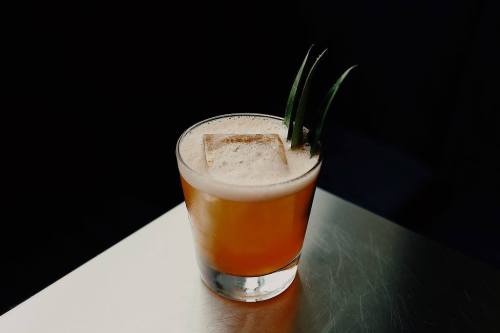 A cocktail in a glass with ice, topped with three green garnishes, set against a dark background.