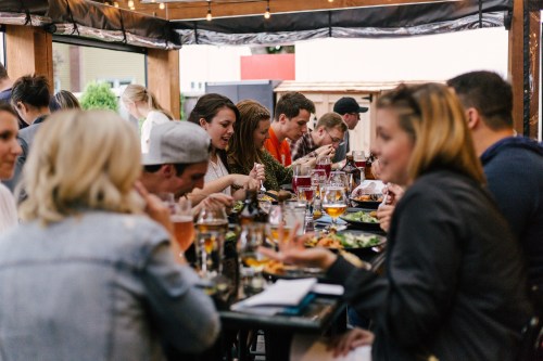 A group of people enjoying a meal together at an outdoor restaurant, with food and drinks on the table.