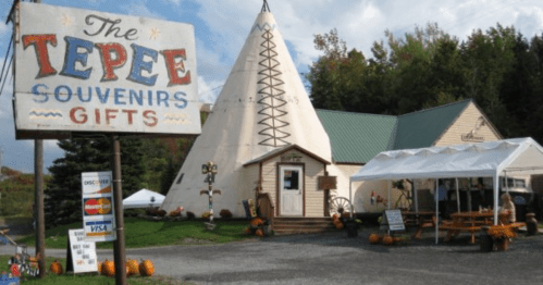 A large teepee-shaped building with a sign reading "The Tepee Souvenirs Gifts" and a small outdoor seating area.