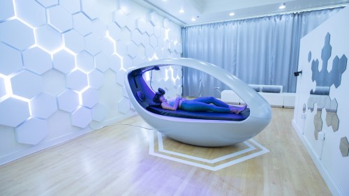 A person relaxes in a futuristic pod in a modern, well-lit room with hexagonal wall designs.