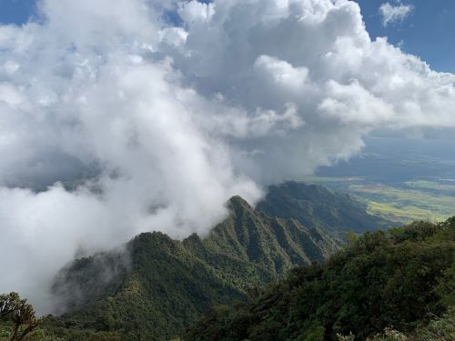 A scenic view of lush green mountains shrouded in clouds under a bright blue sky.