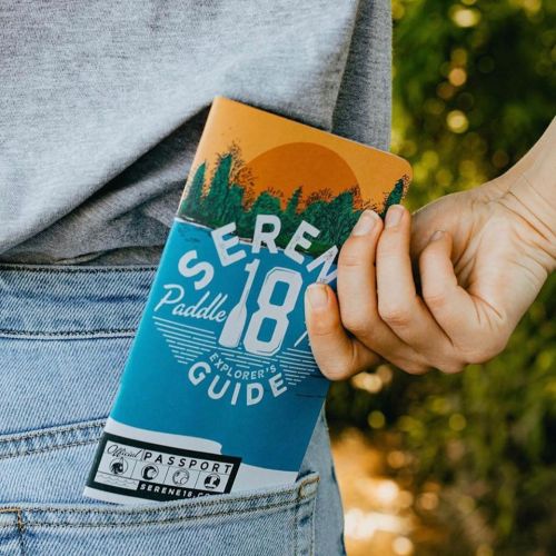 A person places a colorful paddle guide into their back pocket, surrounded by greenery.