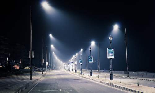 A deserted street at night, illuminated by streetlights, with posters on poles lining the road.