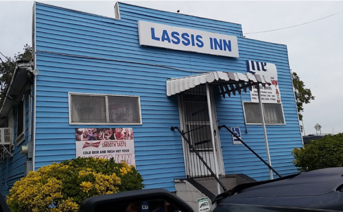 A blue building with a sign reading "Lassis Inn," featuring a staircase and greenery in front.