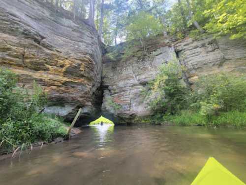 A serene river scene with towering rock formations and lush greenery, viewed from a kayak.